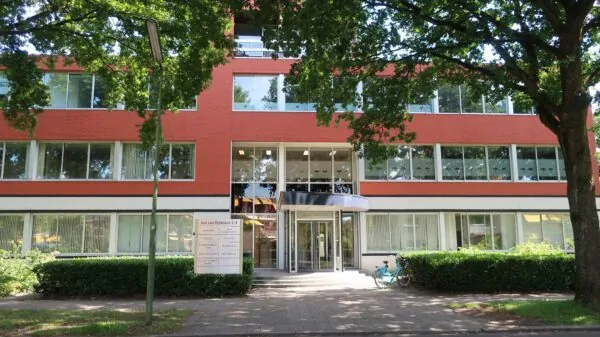 Vooraanzicht van een modern kantoorgebouw aan de Jan van Eycklaan 2-4, omgeven door bomen en een trottoir.